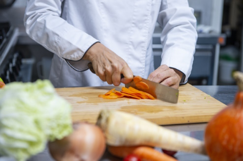 cortando-zanahoria-con-tabla-y-cuchillo-encima-de-mesa-con diferentes-verduras